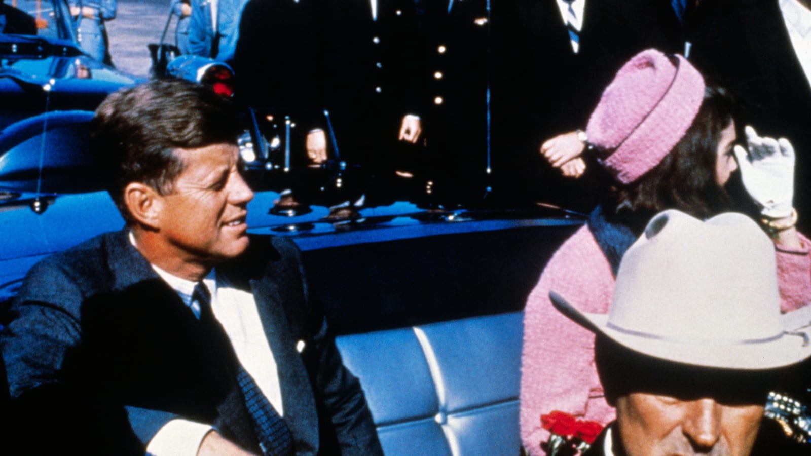 US President John F Kennedy (left), First Lady Jacqueline Kennedy (in pink), and Texas Governor John Connally ride in a motorcade from the Dallas airport into the city.