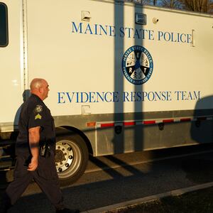 A cop walks in front of a Maine State Police evidence response team vehicle.