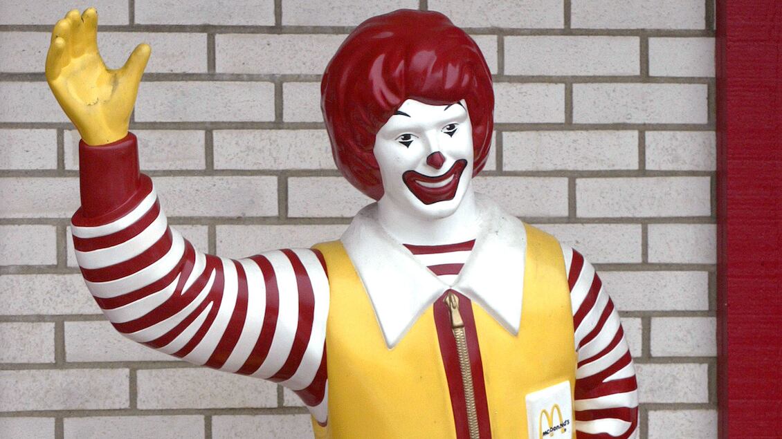 A picture of a Ronald McDonald statue sitting on a bench outside a McDonald’s restaurant.