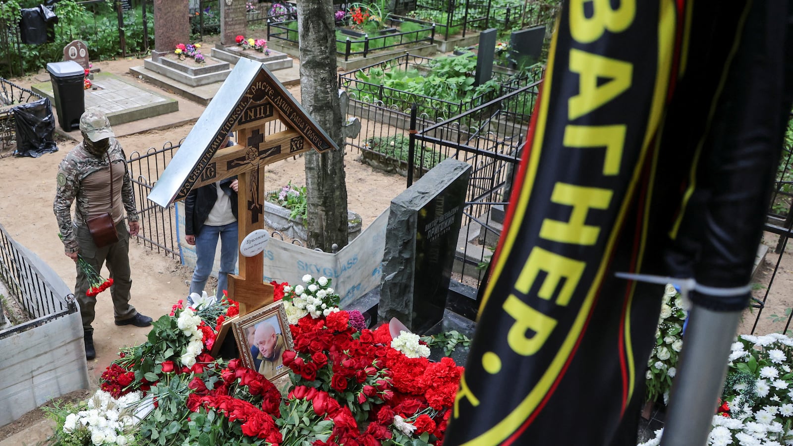 People stand in front of the grave of Russian mercenary chief Yevgeny Prigozhin, with a flag displaying the logo of Wagner private military group seen in the foreground, at the Porokhovskoye cemetery in St. Petersburg, Russia, Aug. 30, 2023.