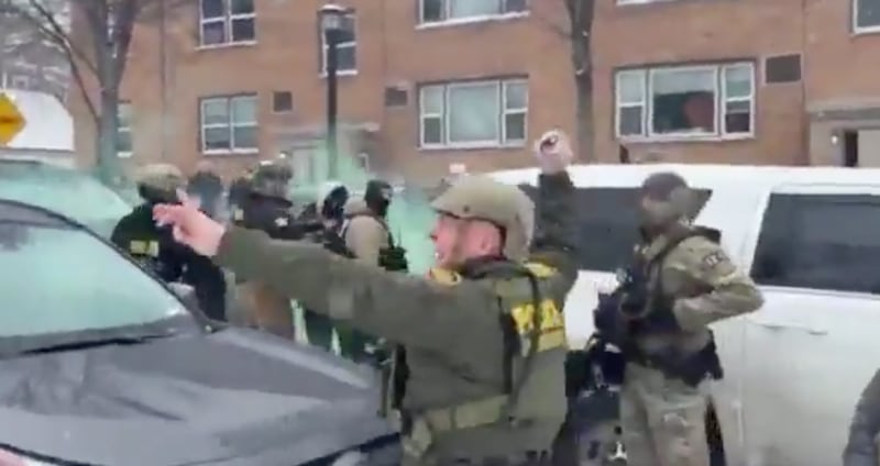 Bovino goes to throw the canister at protesters.