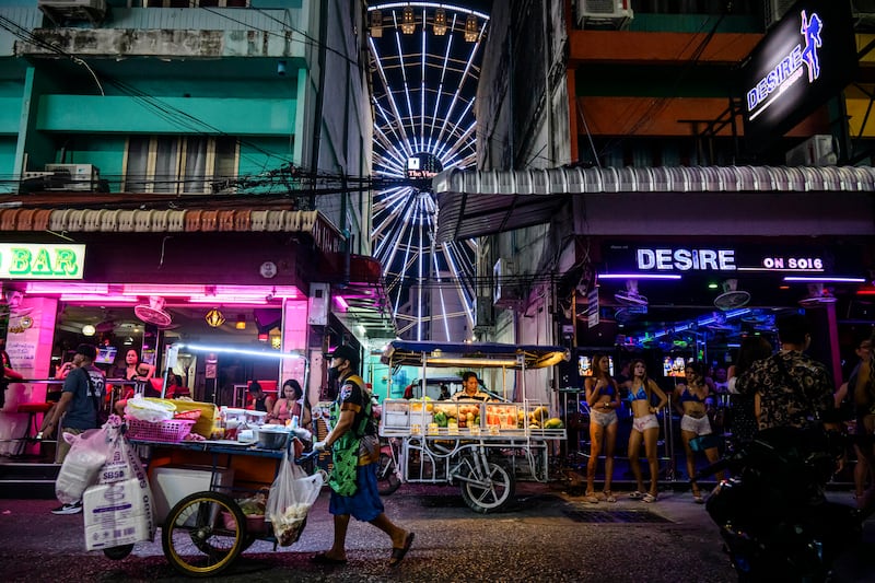 A street vendor pushes his cart past bars and clubs along a street in Pattaya on July 2, 2026. Scantily dressed and wearing stiletto heels, hundreds of girls, some apparently very young, form a seedy guard of honour under the lights of Soi 6, a street in one of Pattaya's red-light districts. (Photo by ANTHONY WALLACE / AFP via Getty Images) / TO GO WITH: Thailand-Australia-crime-tourism-prostitution