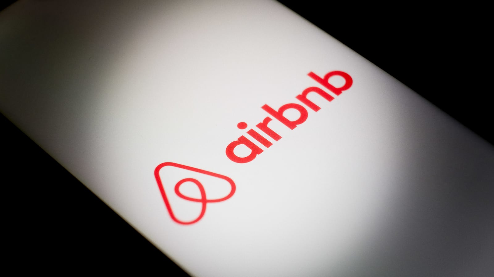 The Airbnb logo is displayed on a smartphone screen.