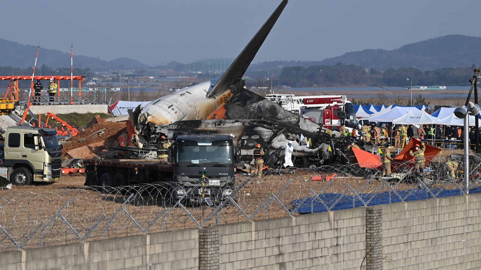 TOPSHOT - Firefighters and rescue personnel work near the wreckage of a Jeju Air Boeing 737-800 series aircraft after the plane crashed and burst into flames at Muan International Airport in South Jeolla Province, some 288 kilometres southwest of Seoul on December 29, 2024. A Jeju Air plane carrying 181 people from Bangkok to South Korea crashed on arrival December 29, colliding with a barrier and bursting into flames, with only two survivors rescued so far and 120 confirmed dead. (Photo by JUNG YEON-JE / AFP) (Photo by JUNG YEON-JE/AFP via Getty Images)