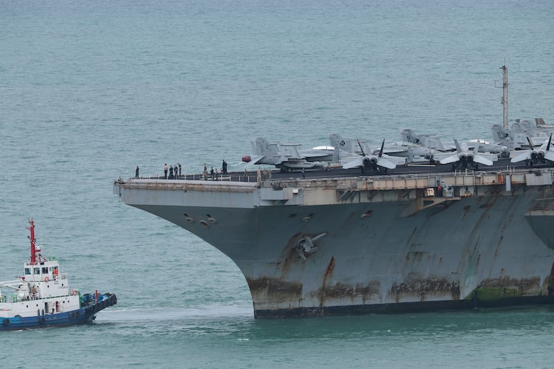 Personnel and aircraft on the deck of the Abraham Lincoln as rust is seen on its underside.