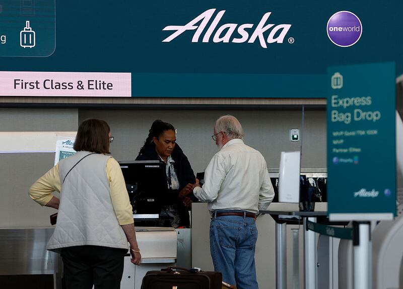 SAN FRANCISCO, CALIFORNIA - JUNE 04: An Alaska Airlines worker helps people check in for a flight at San Francisco International Airport on June 04, 2025 in San Francisco, California. Alaska Airlines is delaying the delivery of two Embraer E175 planes from Brazilian manufacturer Embraer due to tariffs imposed by the Trump administration, and says it will not accept additional costs imposed by tariffs. (Photo by Justin Sullivan/Getty Images)