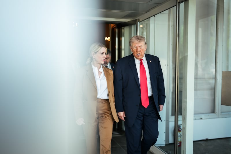 Trump and Pam Bondi. Trump is wearing a dark suit, white shirt and red tie. Bondi is wearing a camel-colored pant suit and white shirt. They are walking through a door at the exit to a building.