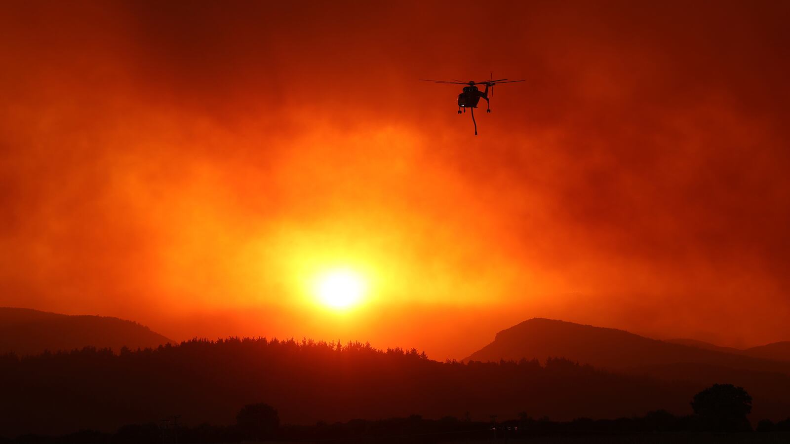 A firefighting helicopter flies away after a water drop as a wildfire burns near the village of Avantas in the region of Evros, Greece, Aug. 21, 2023.