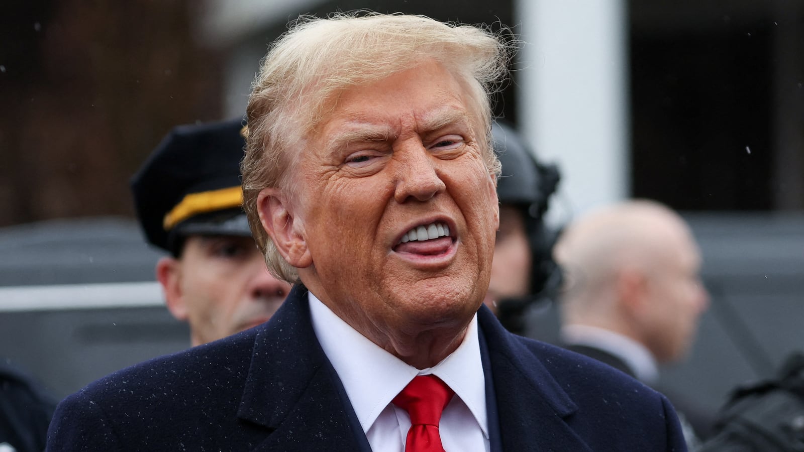 Donald Trump, wearing a suit and red tie, speaks in front of police officers.