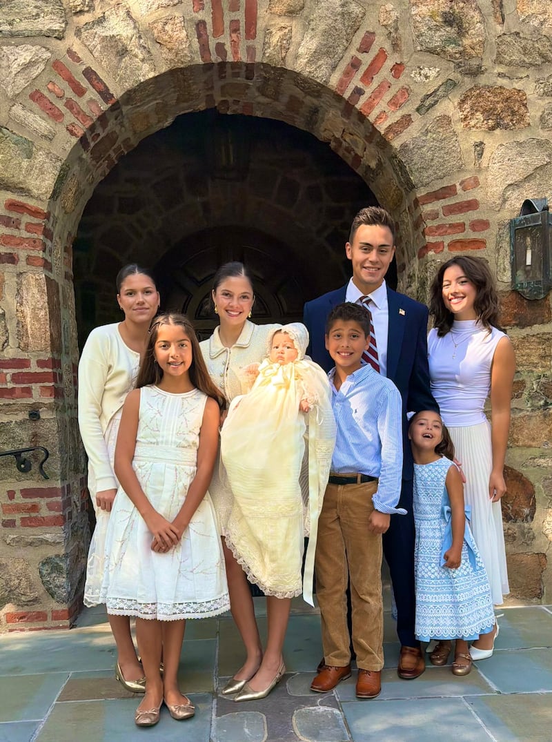 A group of young women and young men, one holding a baby in a christening robe.
