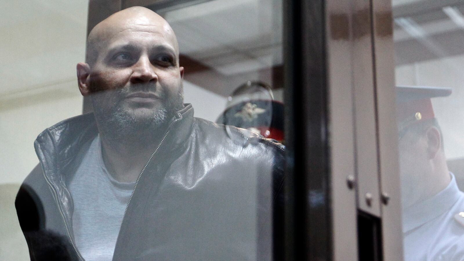 "One of the defendants in the murder trial of Russian journalist and human rights activist Anna Politkovskaya, Sergei Khadzhikurbanov is escorted into a glass-walled cage before a court hearing in Moscow,