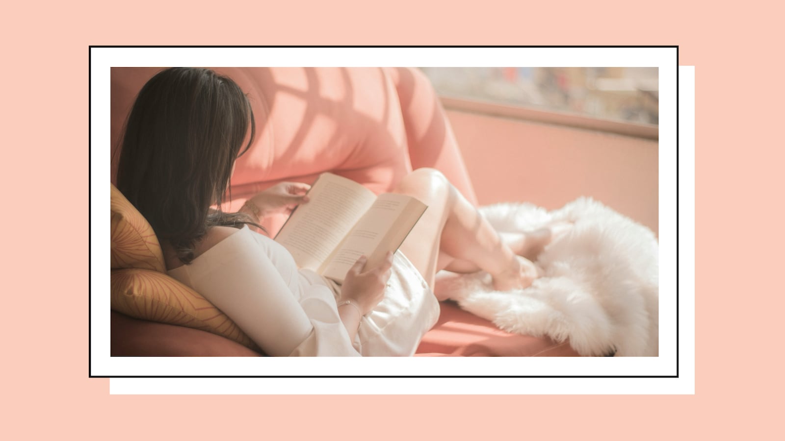 A woman reads a book on a couch in the afternoon, wrapped in a fur blanket.