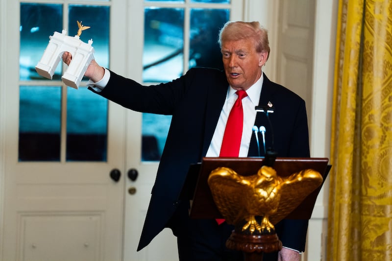 President Donald Trump holds up a model of an arch while delivering remarks during a ballroom fundraising dinner in the East Room of the White House on Wednesday October 15, 2025.