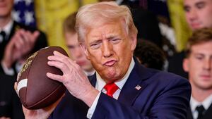 U.S. President Donald Trump, accompanied by Navy Midshipmen co-captain Linebacker Colin Ramos (R), holds up a football presented to Trump during a presentation ceremony for the Commander-in-Chief Trophy to the Navy Midshipmen football team in the East Room of the White House April 15, 2025 in Washington, DC.