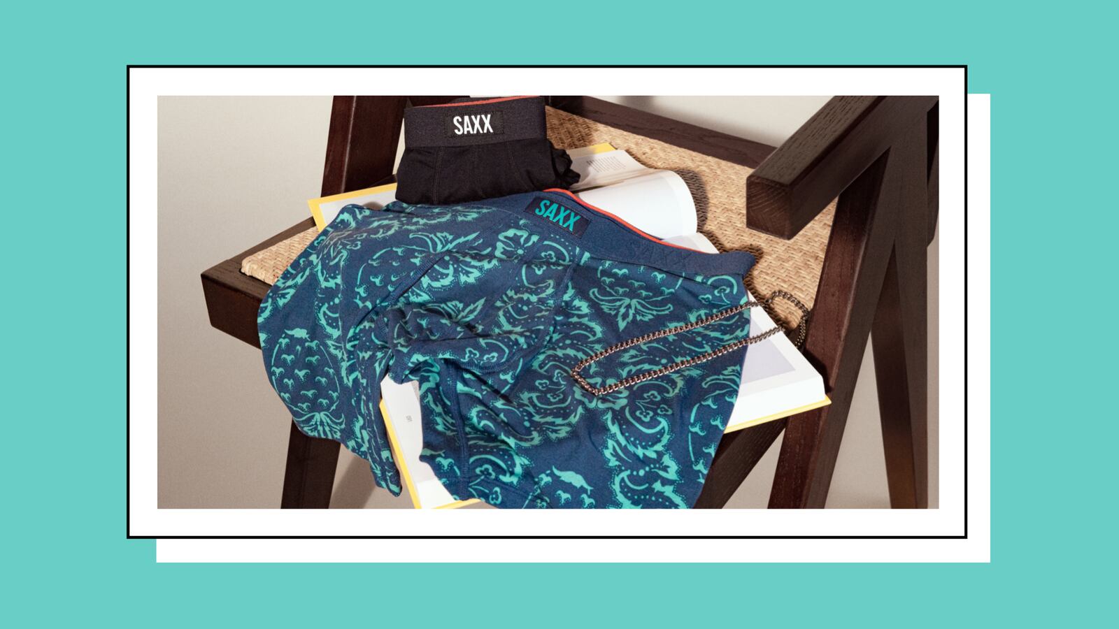 Two pairs of underwear on a chair. They are lying on top of an open book. One pair is colored black and folded neatly. The other is colored dark and light blue and laid out