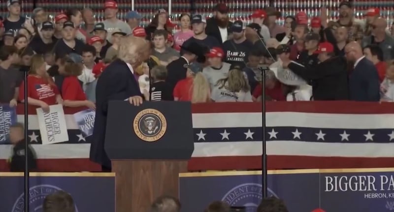 Trump looks on after a woman faints behind him.
