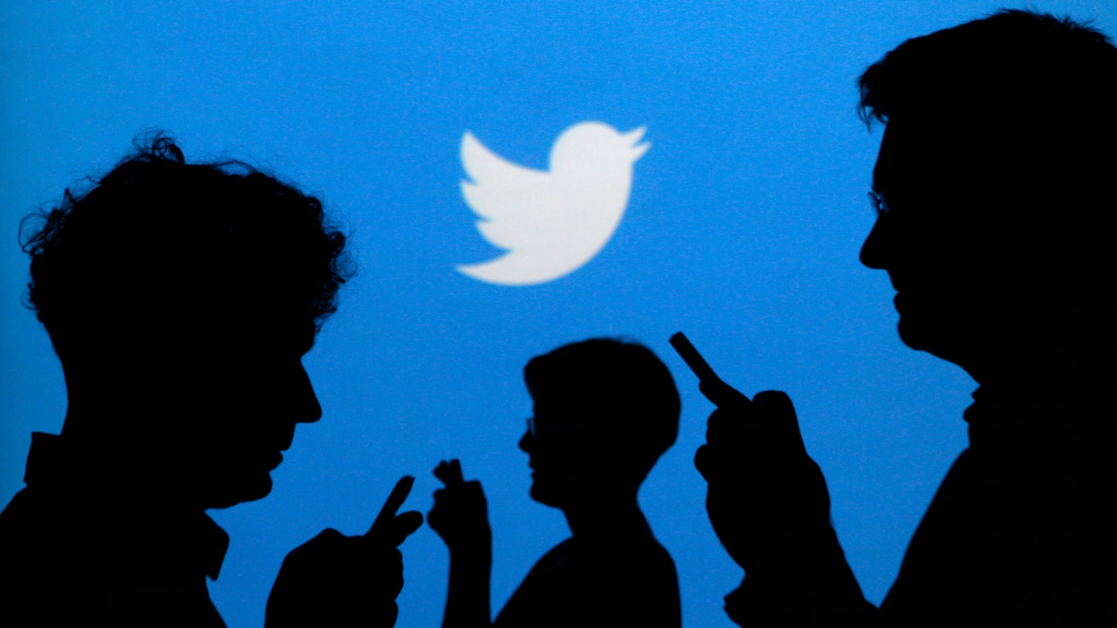 People holding mobile phones are silhouetted against a backdrop projected with the Twitter logo in this illustration picture taken in Warsaw September 27, 2013.