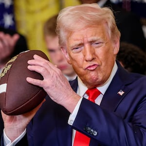 U.S. President Donald Trump, accompanied by Navy Midshipmen co-captain Linebacker Colin Ramos (R), holds up a football presented to Trump during a presentation ceremony for the Commander-in-Chief Trophy to the Navy Midshipmen football team in the East Room of the White House April 15, 2025 in Washington, DC.