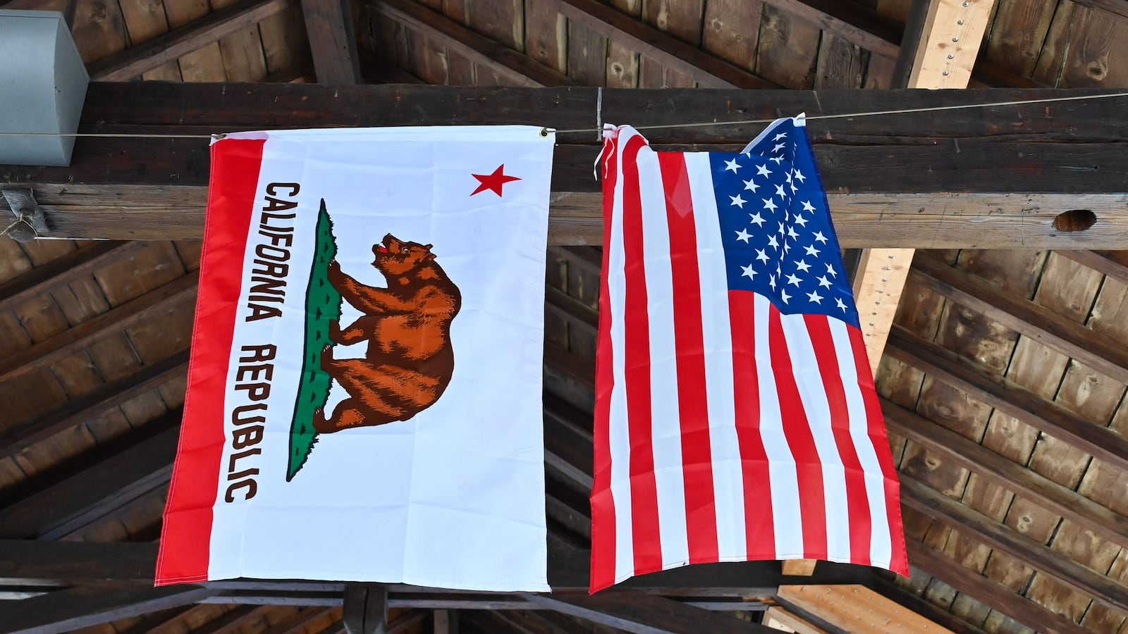 An American flag and a California flag hang from a beam inside a building during the Samoens American Festival in Samoens, Haute Savoie, France, June 29, 2024. (Photo by Matthieu Delaty / Hans Lucas / Hans Lucas via AFP) (Photo by MATTHIEU DELATY/Hans Lucas/AFP via Getty Images)