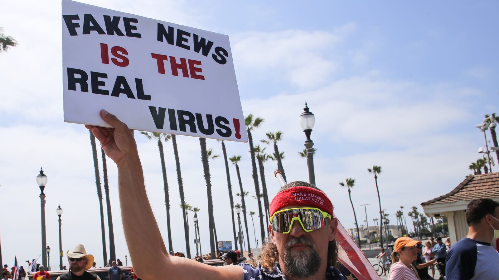 A protester holds a placard that says Fake News Is The Real Virus during the demonstration. Citizens staged a protest in front of the Huntington Beach Pier to demand for the reopening of the California economy.