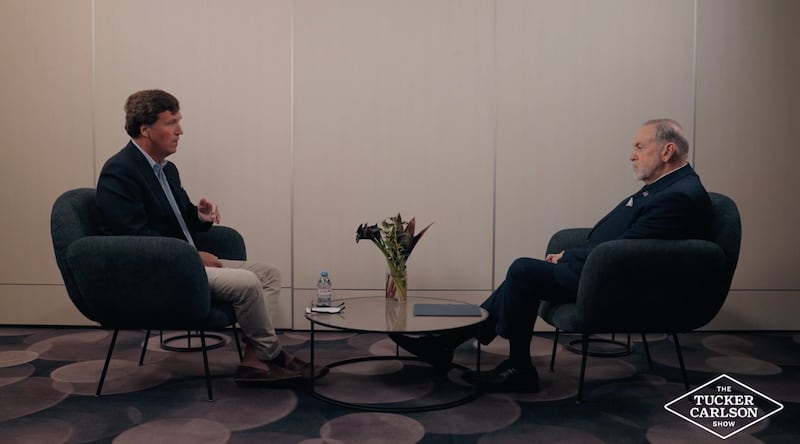 Two men sit facing each other between a coffee table with flowers.