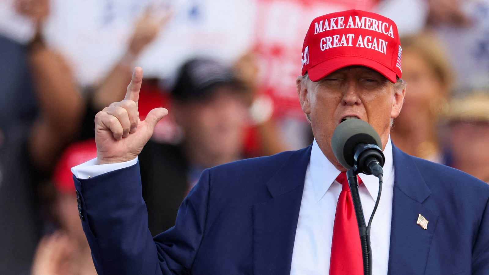 Donald Trump raises his hand while speaking on stage.