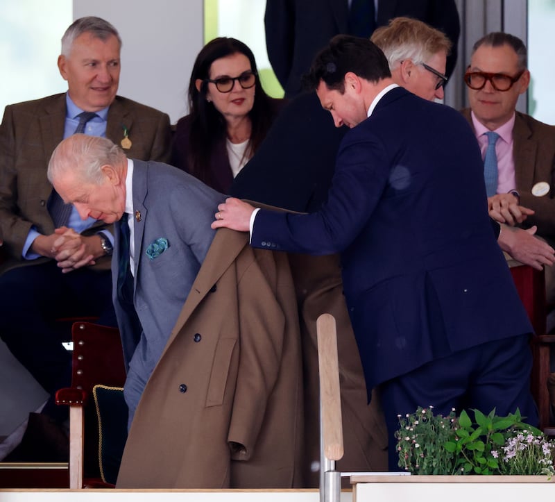 WINDSOR, ENGLAND - MAY 15: (EMBARGOED FOR PUBLICATION IN UK NEWSPAPERS UNTIL 24 HOURS AFTER CREATE DATE AND TIME) Lieutenant Colonel Jonny Thompson (equerry to King Charles III) helps King Charles III put on his overcoat as they watch 'Azerbaijan - Land of Fire', the 'DAKS Pony Club Mounted Games' and the 'Musical Drive of The King's Troop Royal Horse Artillery' during the evening display in the Castle Arena on day 2 of The Royal Windsor Horse Show 2026 in Home Park, Windsor Castle on May 15, 2026 in Windsor, United Kingdom. (Photo by Max Mumby/Indigo/Getty Images)
