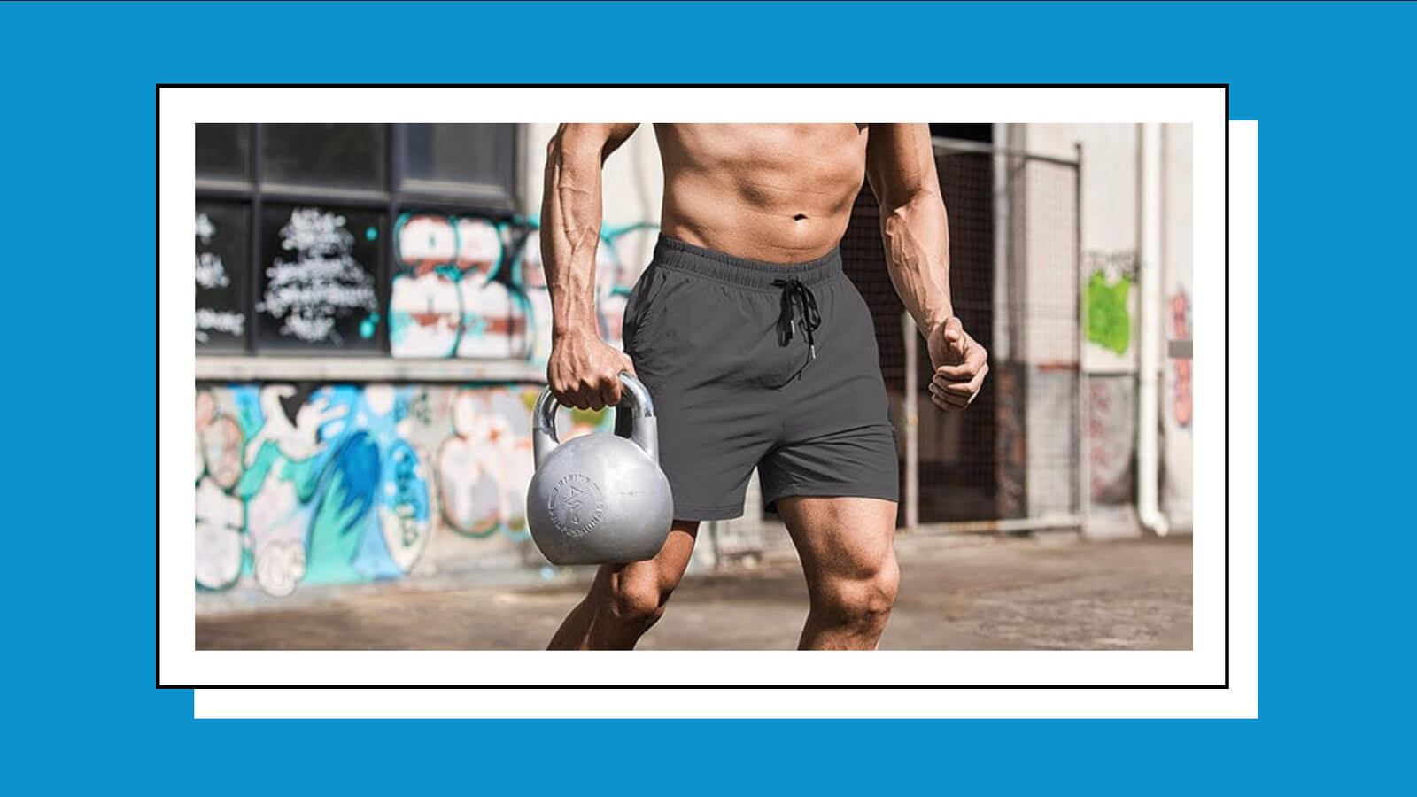 Man wearing shorts and holding a kettlebell in his right hand. He's outside and the wall behind him has graffiti on it.