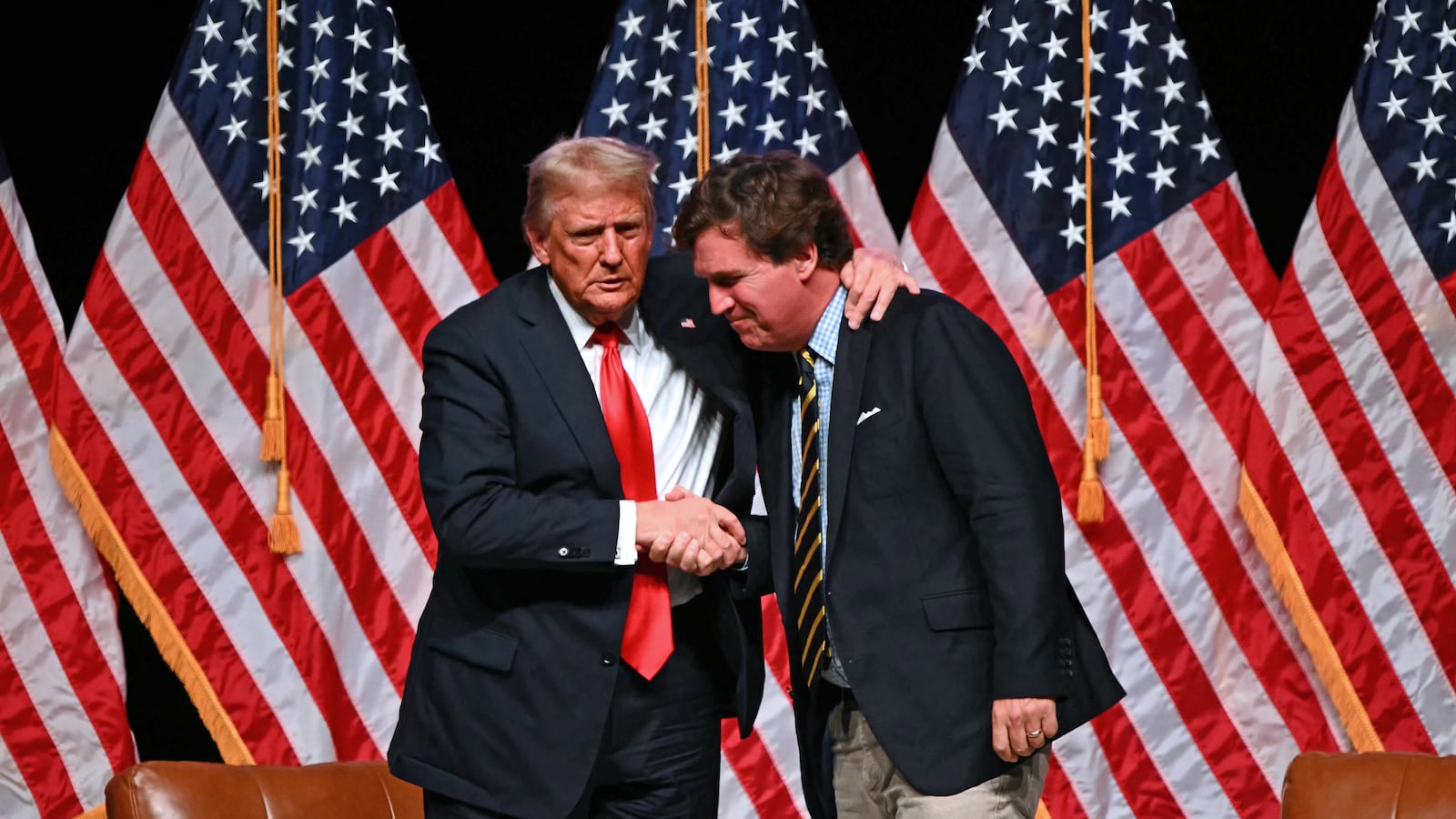 Former US President and Republican presidential candidate Donald Trump (L) shakes hands with US commentator Tucker Carlson at the end of a live interview in the finale of the Tucker Carlson Live Tour at Desert Diamond Arena in Glendale, Arizona, on October 31, 2024. (Photo by Patrick T. Fallon / AFP) (Photo by PATRICK T. FALLON/AFP via Getty Images)