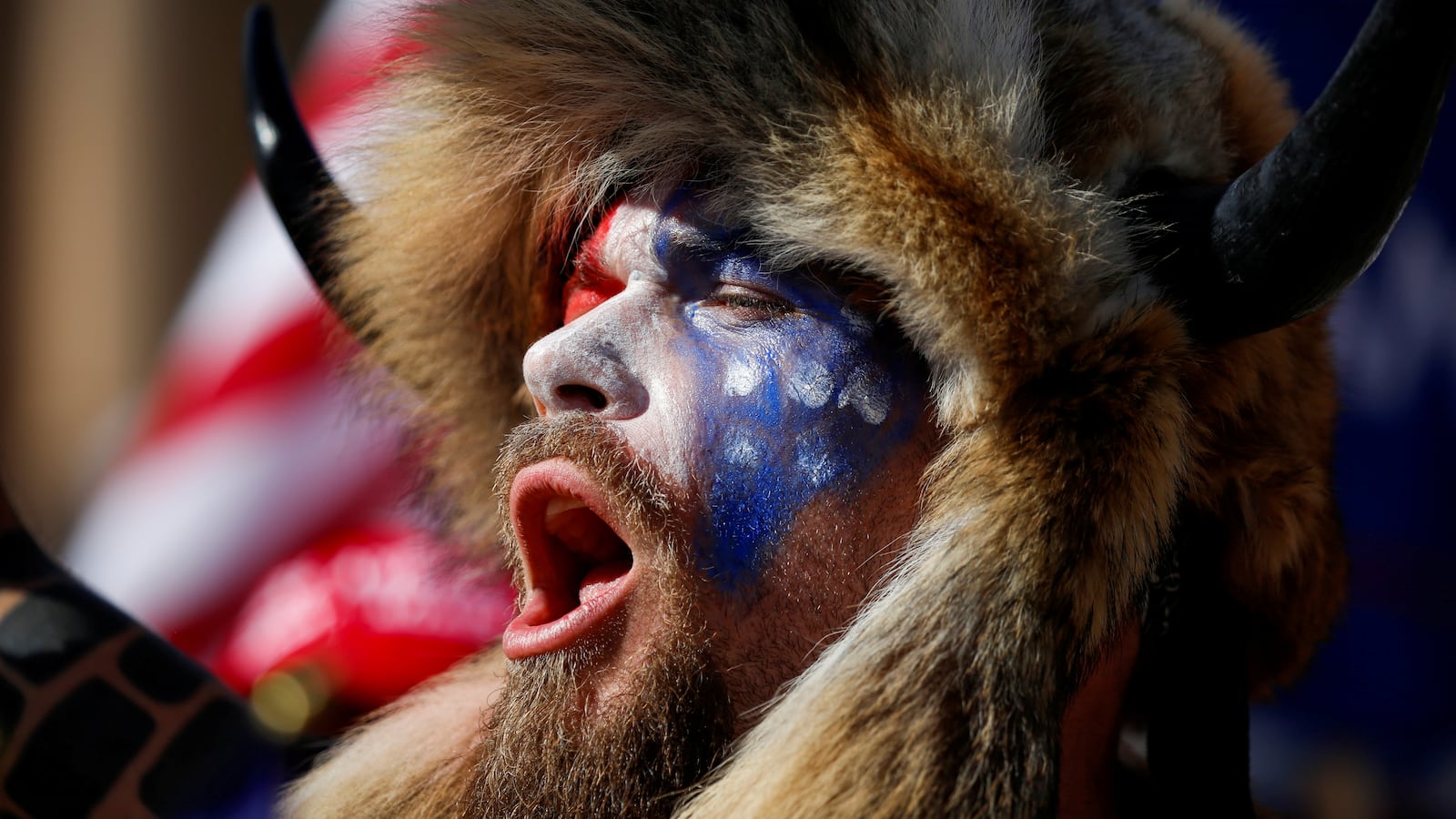 Jacob Chansley, wearing face paint and a fur hat, screams during a protest.