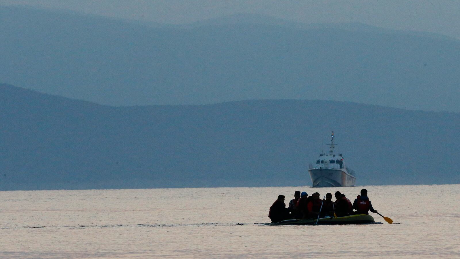 Migrants in a dinghy paddle their way on the Mediterranean Sea to attempt crossing to the Greek island of Kos, as a Turkish Coast Guard ship patrols off the shores off Bodrum, Turkey, September 19, 2015.