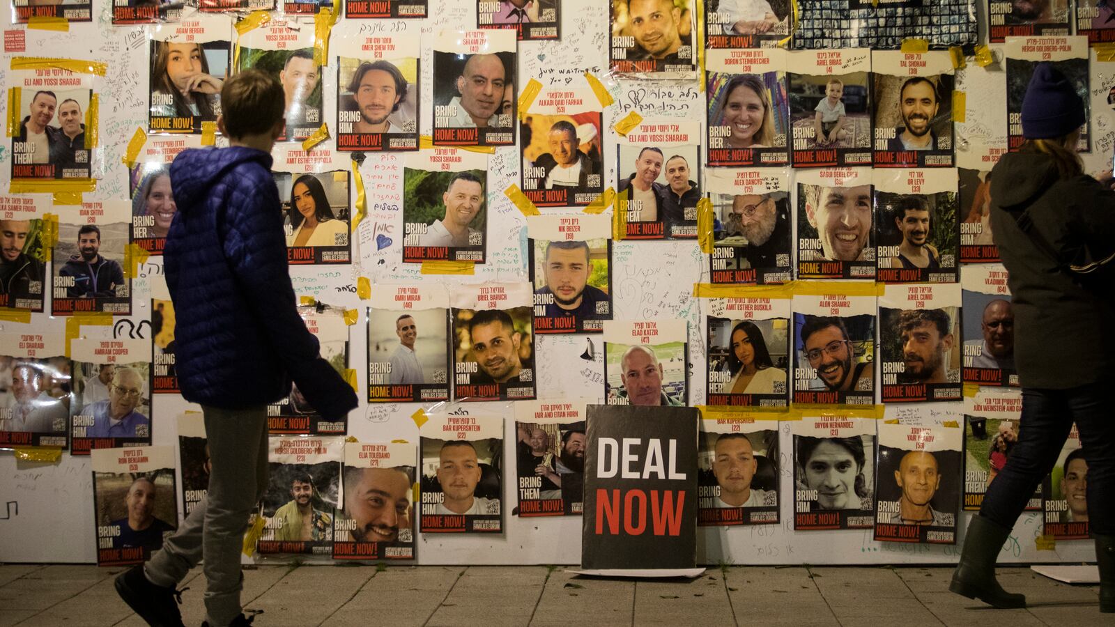 People walk by a wall with photos of hostages held by Hamas during a rally on January 27, 2024 in Tel Aviv.