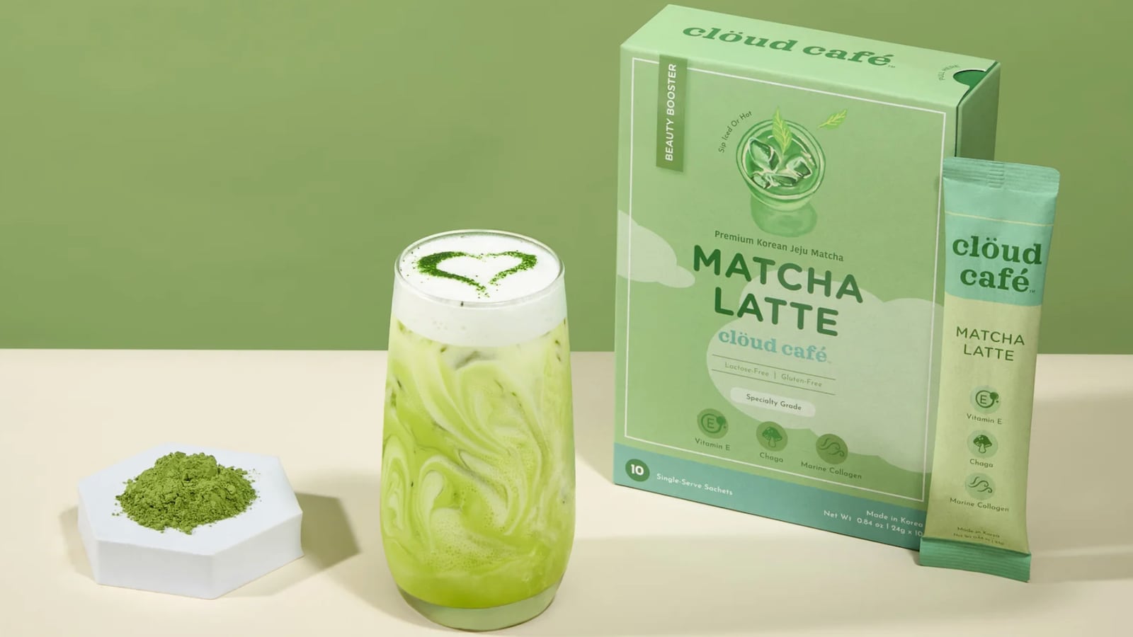 A vibrant green matcha latte in a clear glass, topped with foam and a heart-shaped design made from matcha powder. The background is a light green, complementing the latte's color. Next to the glass is a box labeled "Cloud Café Matcha Latte."