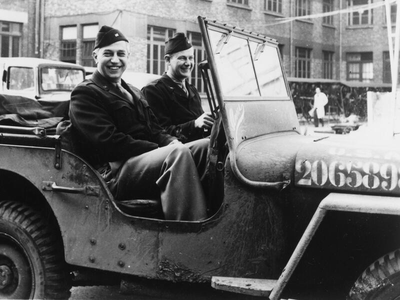 Two men in WWII Army uniform driving a Jeep. The picture is black and white
