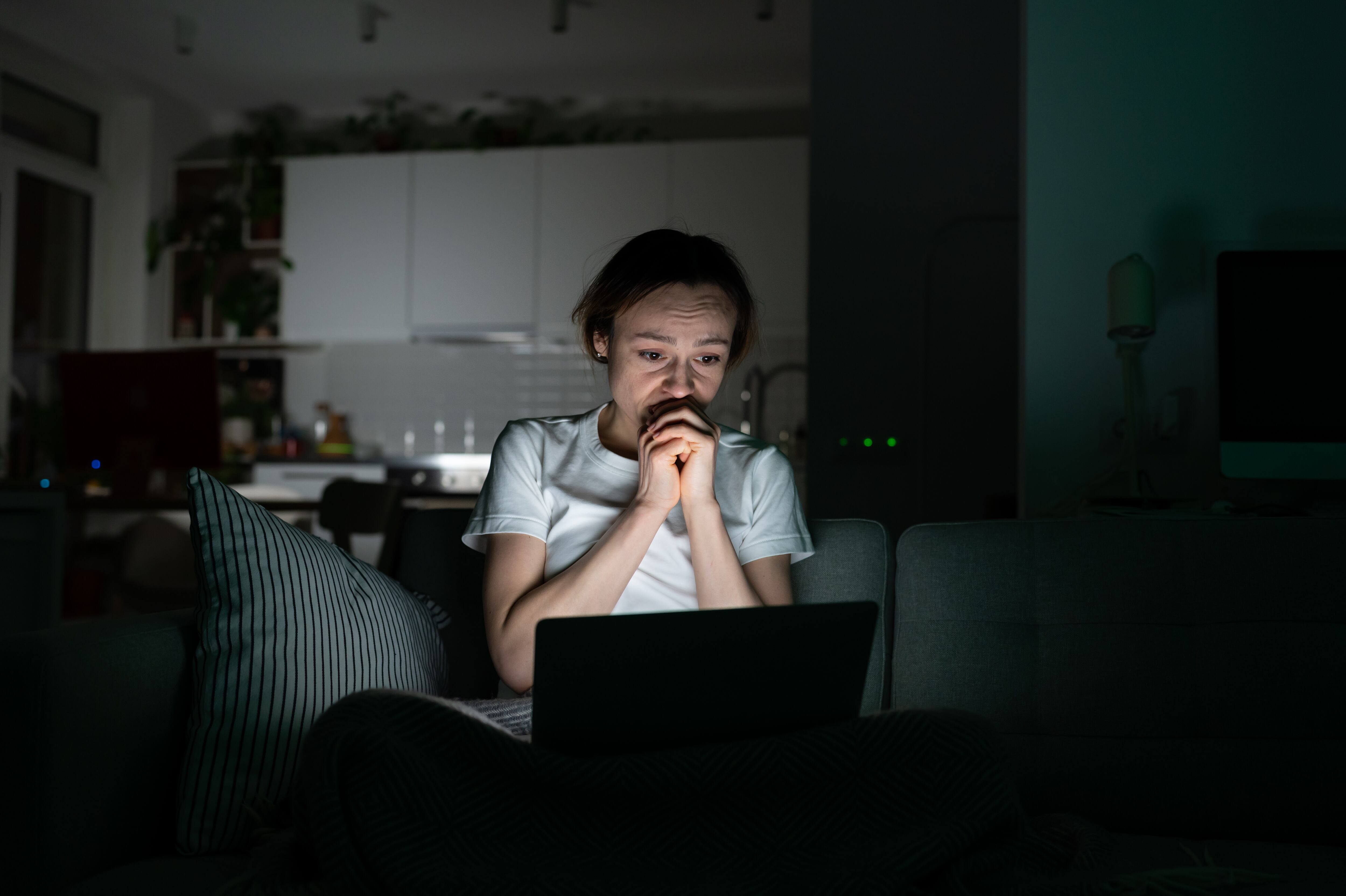 Anxious young woman looking at laptop screen at night, read sudden bad news, very worried. Shocked female can not stop scrolling news media in computer before bedtime. Anxiety, mental health.