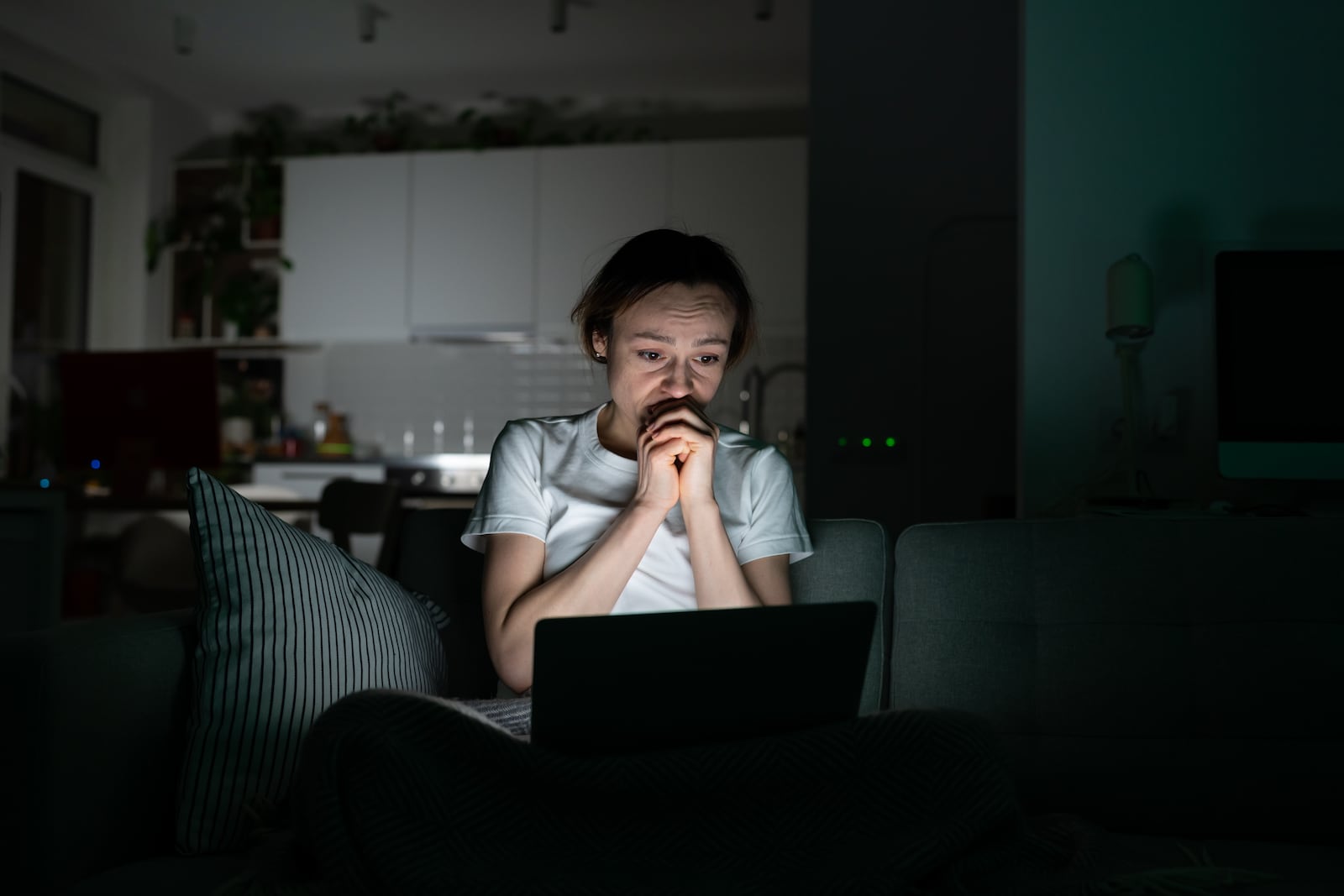 Anxious young woman looking at laptop screen at night, read sudden bad news, very worried. Shocked female can not stop scrolling news media in computer before bedtime. Anxiety, mental health.