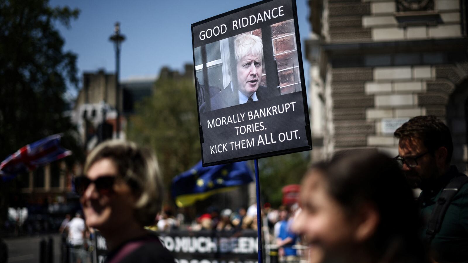 People walk past a placard criticising former Britain's Prime Minister Boris Jonson, during a protest rally outside Palace of Westminster, home of the Houses of Parliament, in Westminster, central London, on June 14, 2023.