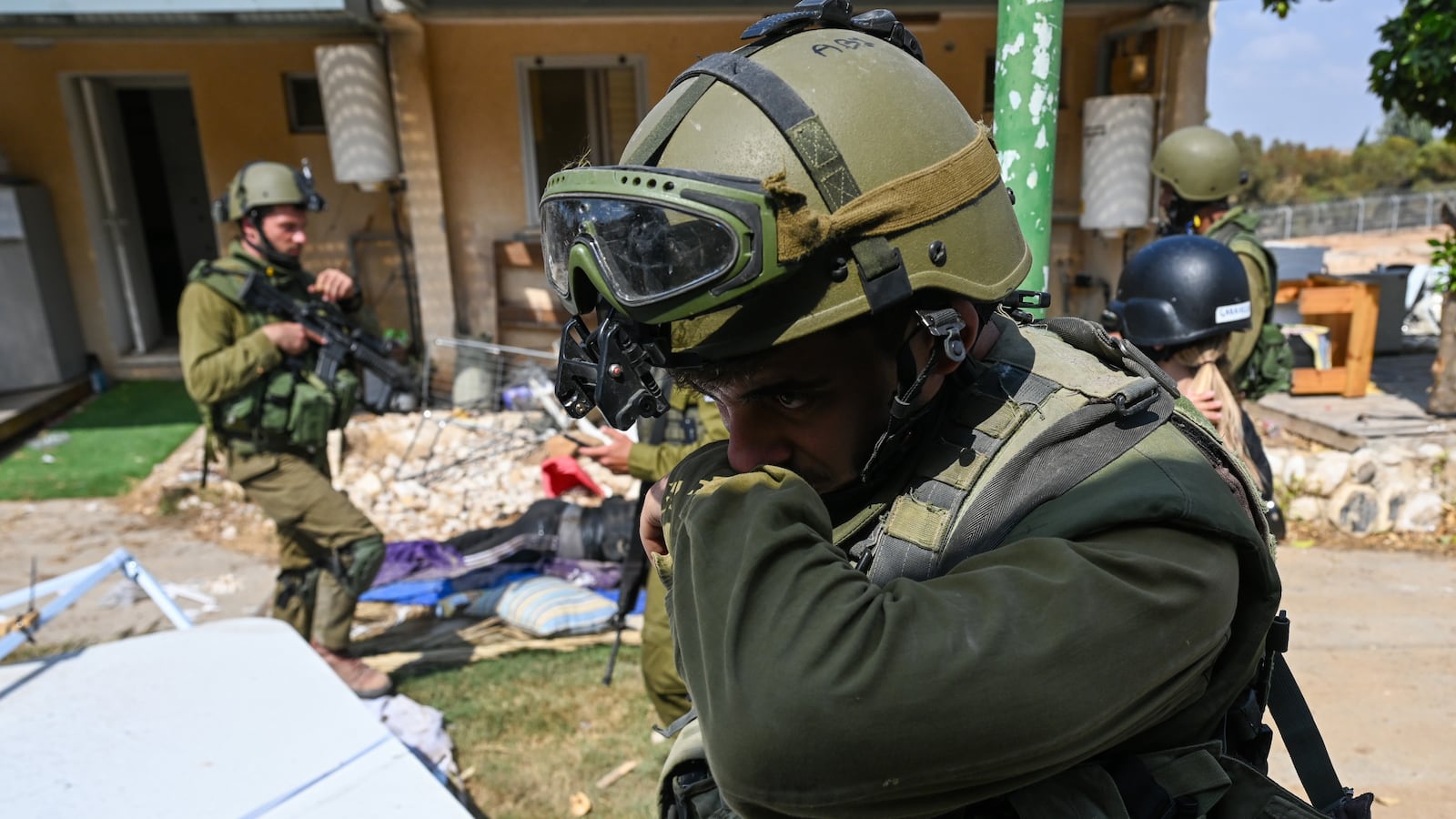 An IDF soldier covering his nose in front of a house.