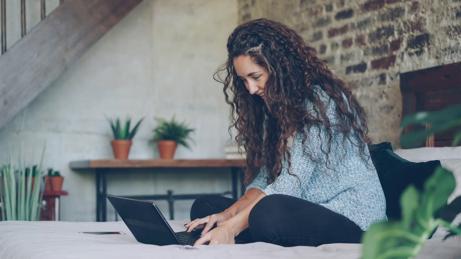 A woman using her laptop while sitting in her bed.