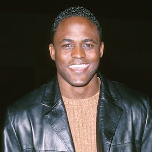 Wayne Brady wearing a black leather jacket and brown sweater in 2000.