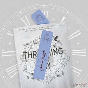 A light blue "On The Same Page" bookmark with a line drawing of a person reading rests on a gray and white book cover featuring clouds, a dragon, and the tagline "Thirteen unforgettable stories. One legendary day." A clock face fills the background.